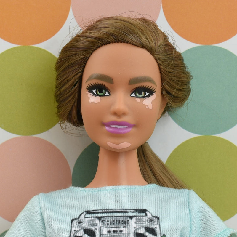 Headshot of a curvy Barbie doll with vitiligo and brown hair named Carmen