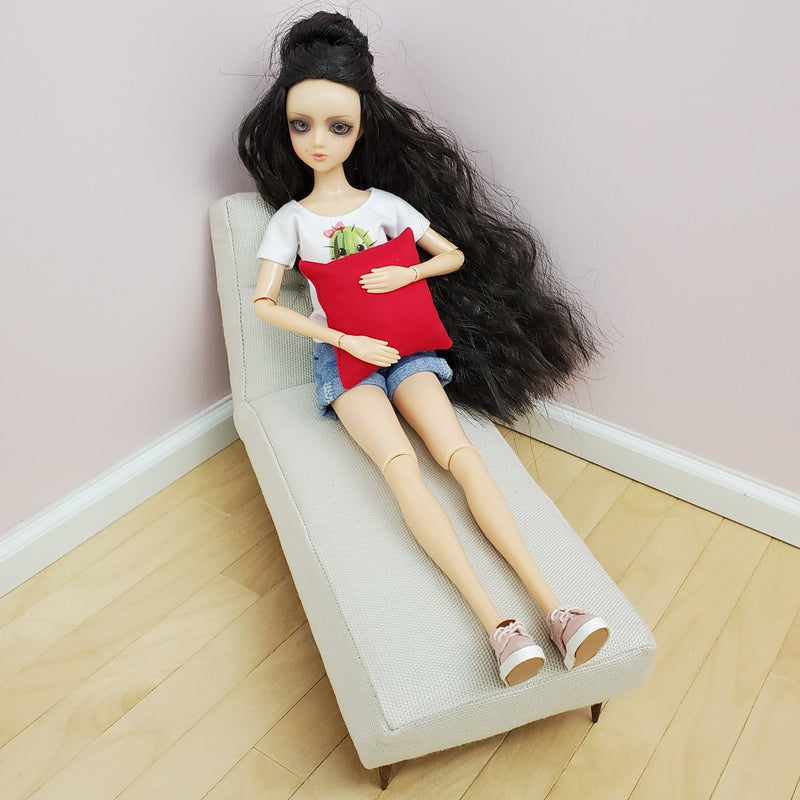 J-doll holding 2x2 square pillow, sitting on a chaise lounge